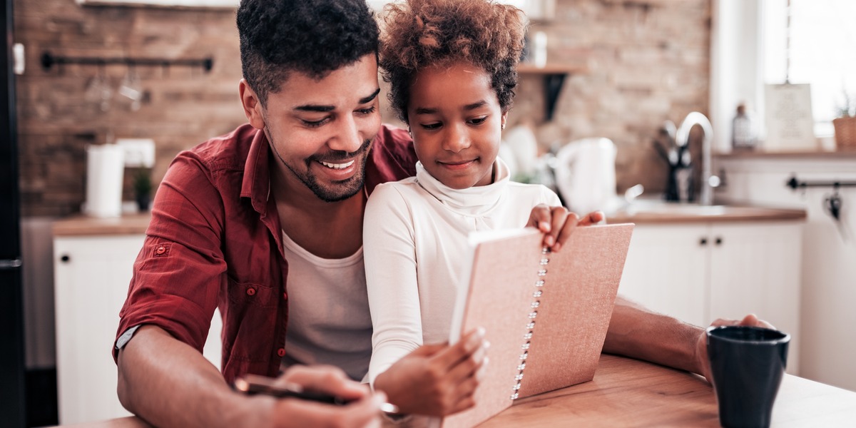 A parent and child reviewing a notebook together at a kitchen table